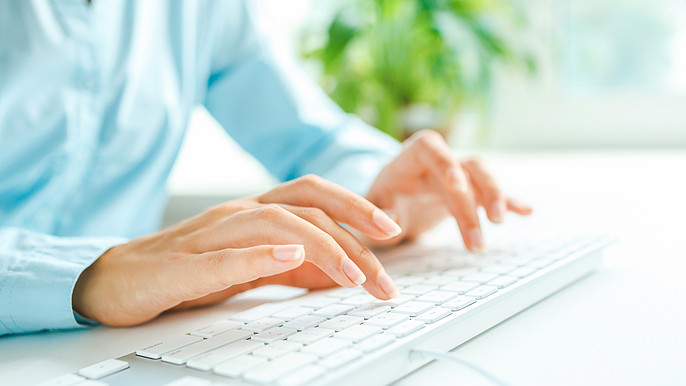 Weiblich gelesene Person mit hellblauer Bluse tippt auf einer weißen Tastatur