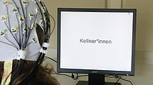 Das Bild zeigt eine Person vor einem Computerbildschirm: Mit am Kopf angebrachten Elektroden wurde die elektrische Aktivität des Gehirns beim Lesen verschiedener Satzkombinationen gemessen