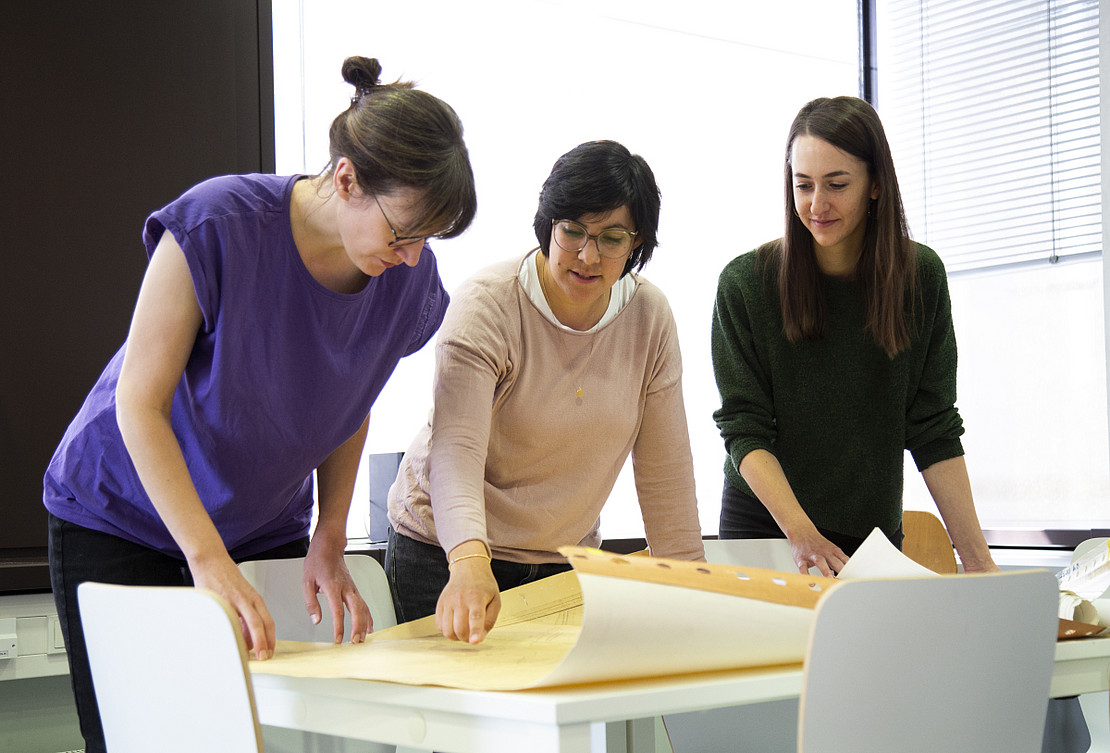 Three people look at and discuss a large construction drawing