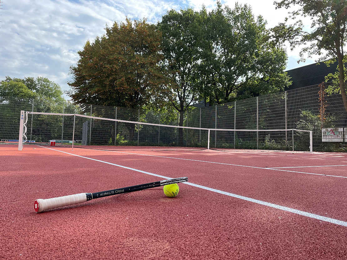 The new tennis court at the Aueparkalle. In the foreground, a tennis racket lies on the floor of the court.